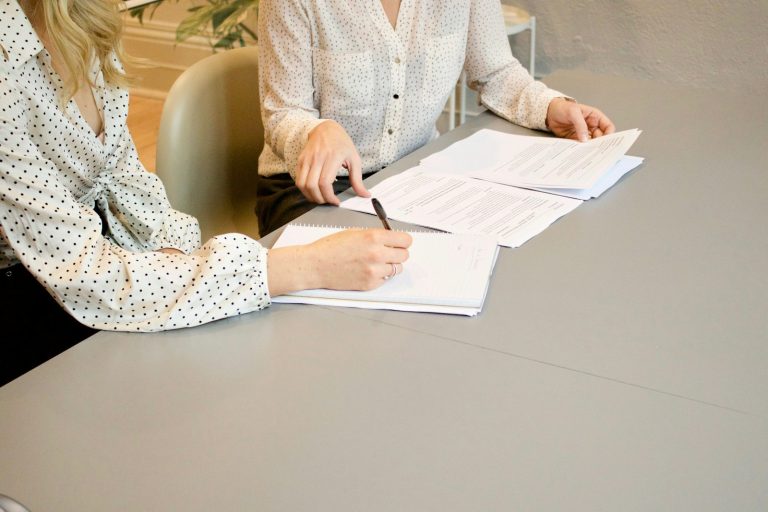Zwei Frauen besprechen und unterschreiben Unterlagen an einem Tisch