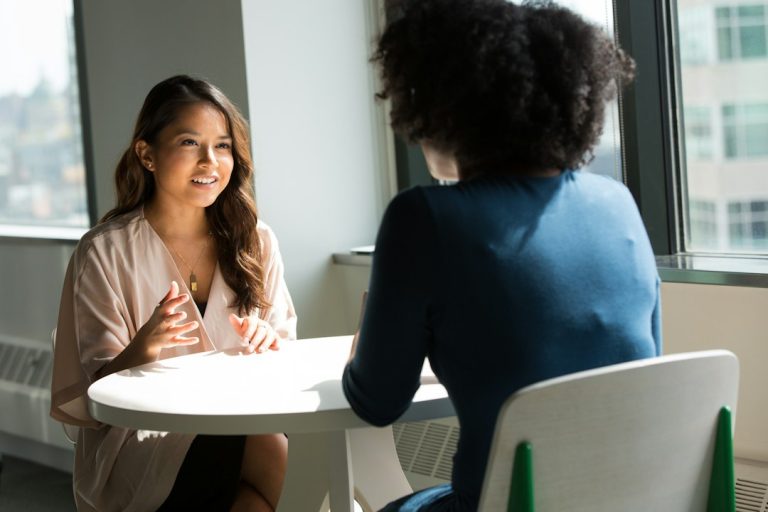 Zwei Frauen sitzen an einem runden Tisch und führen ein persönliches Gespräch
